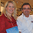 Woman in red, holding a book, stands with two men and a woman in chefs' wear, with a notice about a book signing.