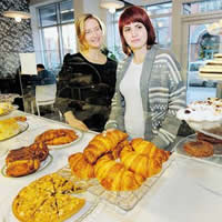 Two women stand behind a white counter covered in delicious-looking golden pastries.