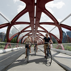 Three bikers smile as they pedal beneath the futuristic red 