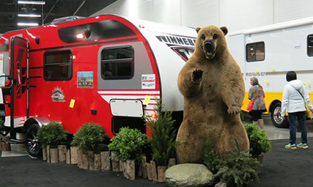 Picture of camper with fake bear standing in front of it. 