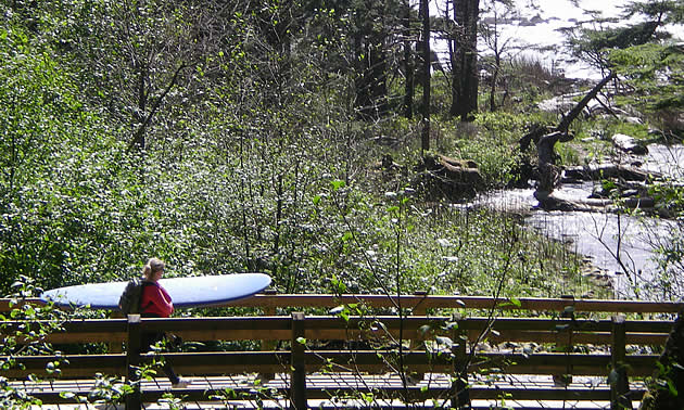 person carrying a surfboard over a bridge