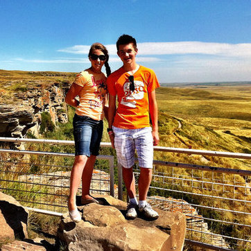 Two people stand on a cliff at the Head-Smashed-In-Buffalo Jump Interpretative Centre. The backdrop is a stunning prairie view over one of the world's oldest, largest and best-preserved buffalo jumps.